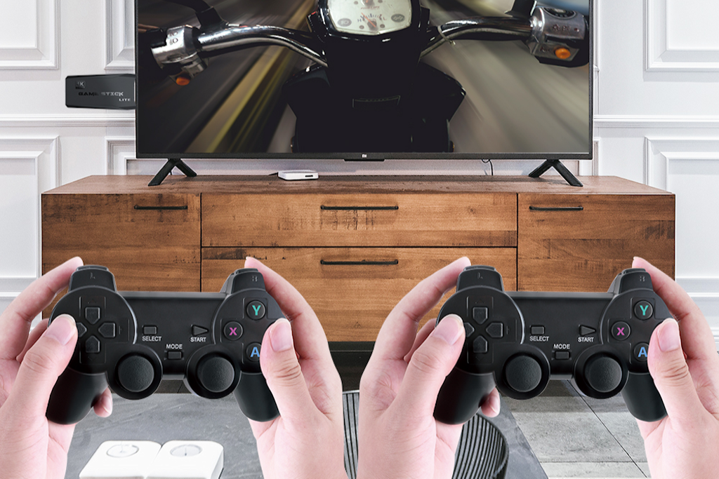 A person holding two wireless controllers with a retro-style game console connected to a TV displaying a racing video game.