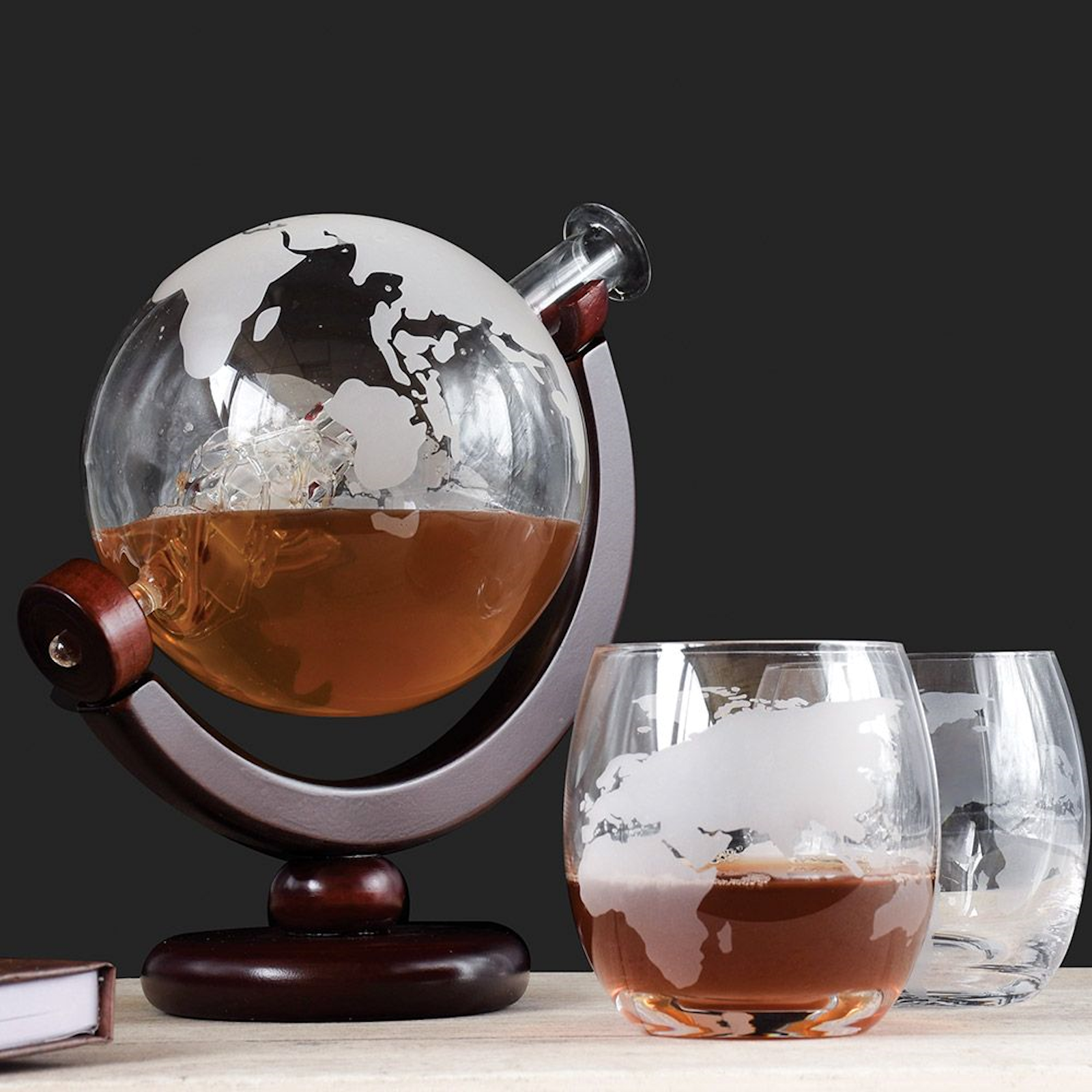 Globe decanter set with 2 matching glasses Decanter is shaped like the world and contains a glass ship Decanter and glasses feature map-style markings Includes a crescent-shaped, wooden stand